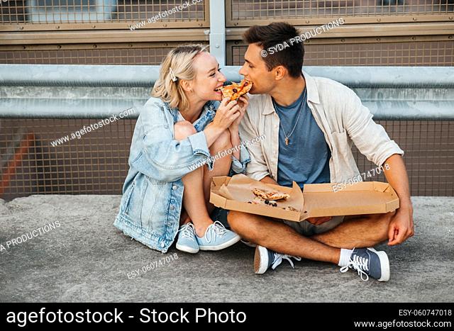 happy couple eating pizza on city roof top parking