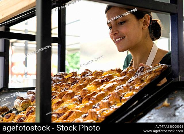 Medium shot of a female Latin-American bakery owner looking at her pastries displayed on a shelf