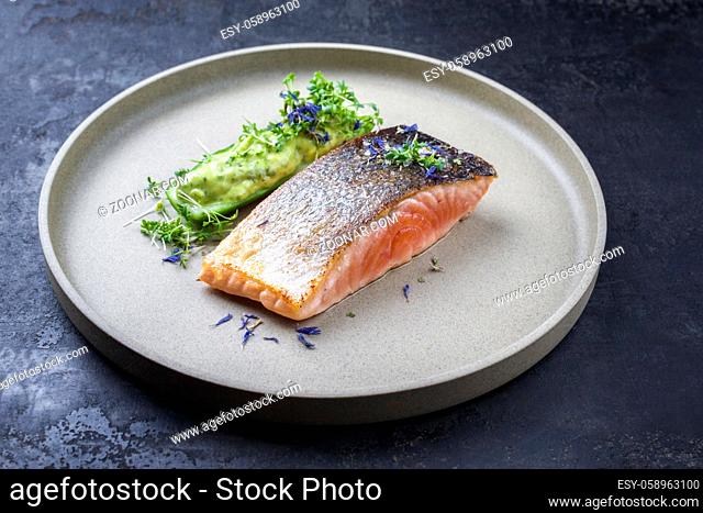Minimalistic design salmon fish filet glazed with avocado and wasabi creme in a sliced cucumber as closeup on a modern design plate decorated with herbs