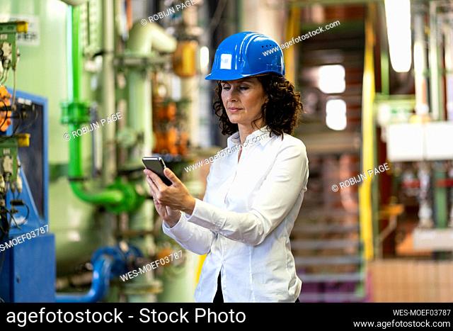 Female engineer with hardhat using mobile phone while standing in industry