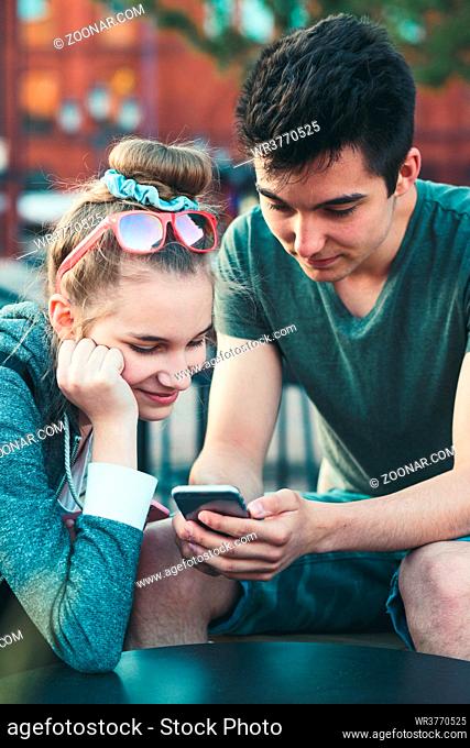 Couple of friends, teenage girl and boy, having fun with smartphones, sitting in center of town, spending time together