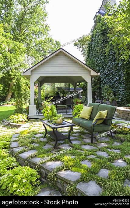 Black cast iron metal and green cushioned loveseat with yellow cushions and coffee table on elevated grey flagstone patio with Sedum rupestre 'Stone orpine' -...