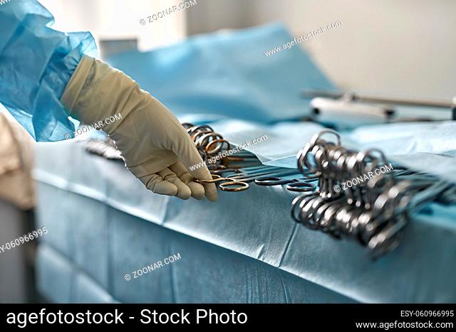 Hand in medical glove is taking a surgical forceps from the table in the operating room. Closeup low aperture photo. Horizontal