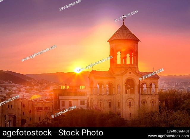 Bell tower of Holy Trinity church or Tsminda Sameba Cathedral sunset panorama and georgian flag in Tbilisi, Georgia
