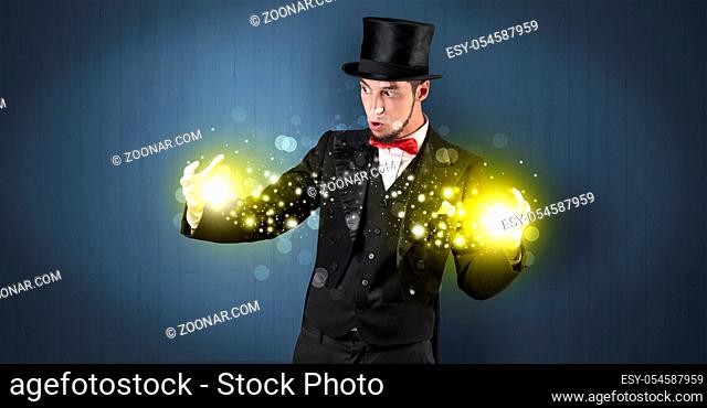 Handsome illusionist holding his superpower on his hands with gold wallpaper