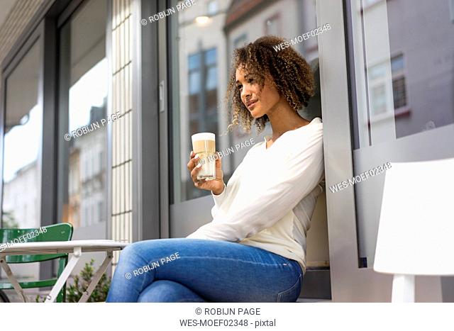 Young woman relaxing at pavement cafe with Latte Macchiato