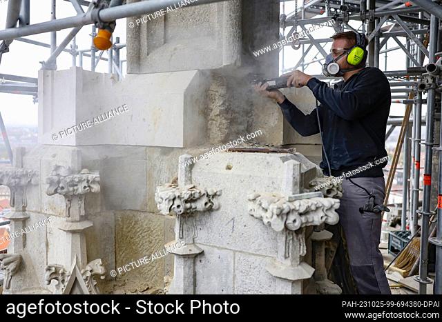 PRODUCTION - 24 October 2023, Bavaria, Regensburg: Stonemason MaximilianLell flext away old sandstone in the tower of Regensburg Cathedral