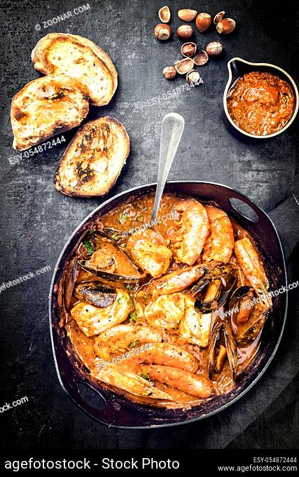 Traditional Catalan fish stew romesco de peix with prawns, mussels and fish as top view in a modern design cast-iron roasting dish