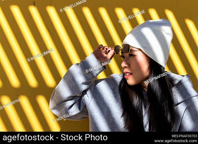 Woman removing sunglasses against yellow wall