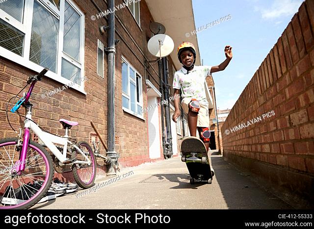 Portrait carefree boy skateboarding in sunny apartment alleyway
