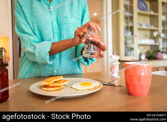 Mid section of woman putting salt on cooked eggs