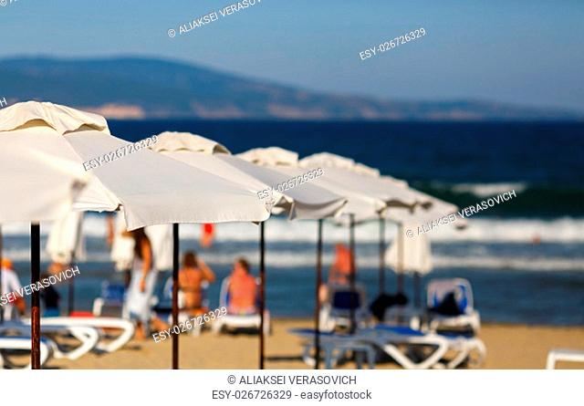 White beach umbrellas on a blurred background of blue sea and the mountains. White parasols. Blurred beach background. Shallow depth of field