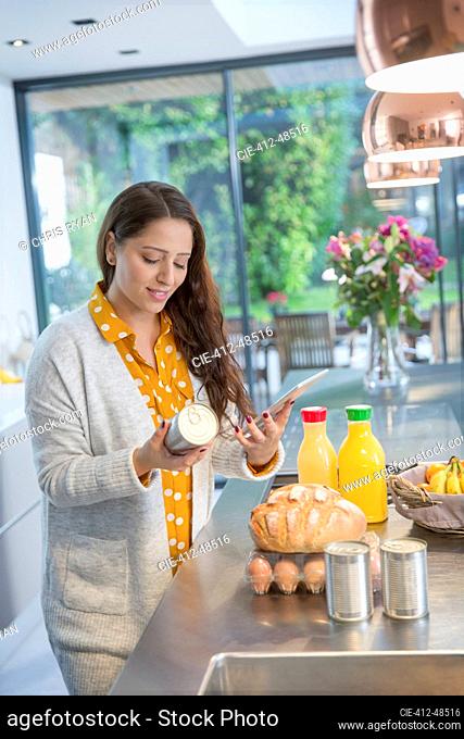 Woman with digital tablet checking food labels in kitchen