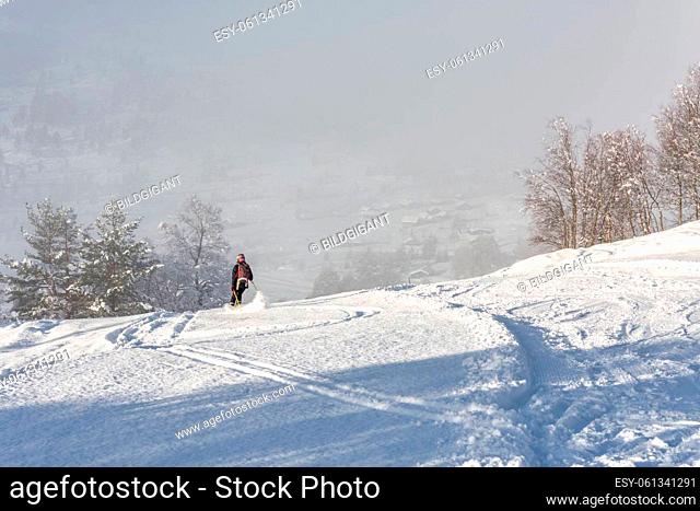 Woman with brown hair, wearing black ski wear and helmet skiing down the top of a mountain, rear view, beautiful snow landscape with trees
