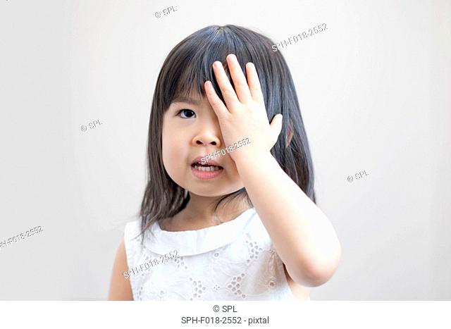 Young girl covering eye with hand, studio shot