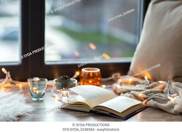 book, garland lights and candles on window sill