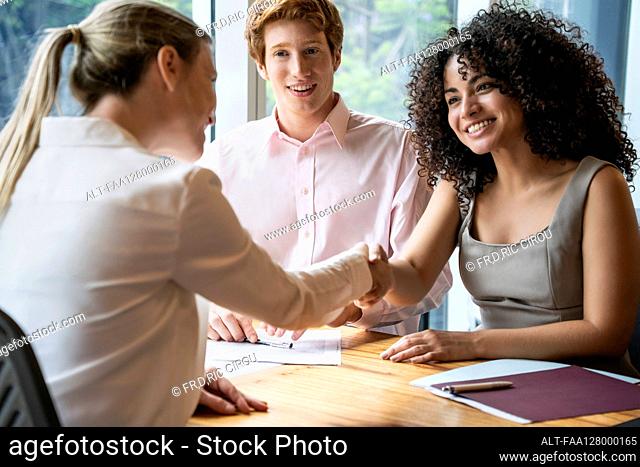 Young couple shaking hands with businesswoman during meeting