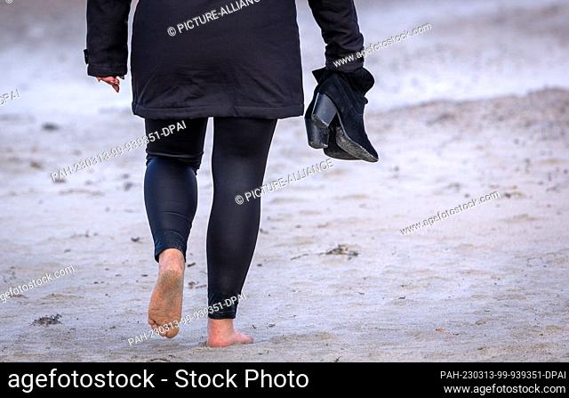 13 March 2023, Mecklenburg-Western Pomerania, Rostock: Barefoot a woman walks on the beach in Warnemünde in stormy weather