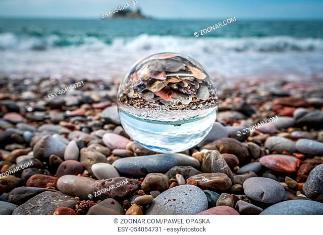 Small stones reflected in large transparent glass ball placed on the beach, coast of Montenegro