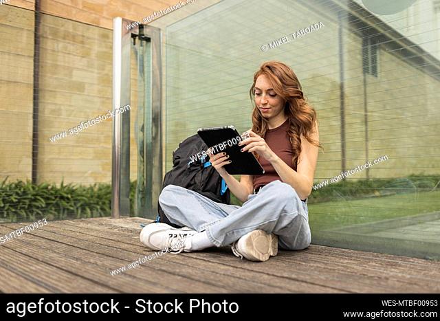 Beautiful woman using digital tablet while sitting by backpack outdoors