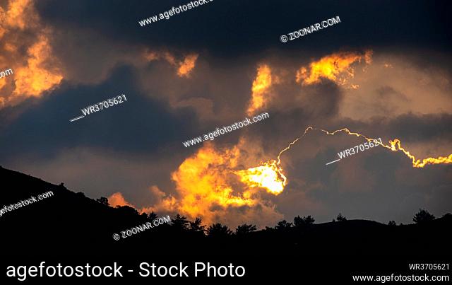 Sunset with stormy cloud sky and hidden sun behind the clouds on the mountains. Troodos Cyprus
