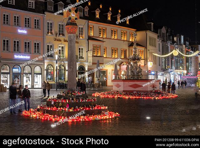 07 December 2020, Rhineland-Palatinate, Trier: In the evening people stand on the main market square, where numerous candles are lit around the market cross and...