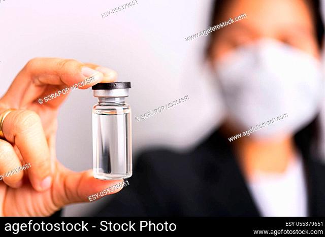 Asian woman doctor wearing surgical protective cloth face mask against coronavirus her hold ampoule bottle vaccine focus on glass transparent