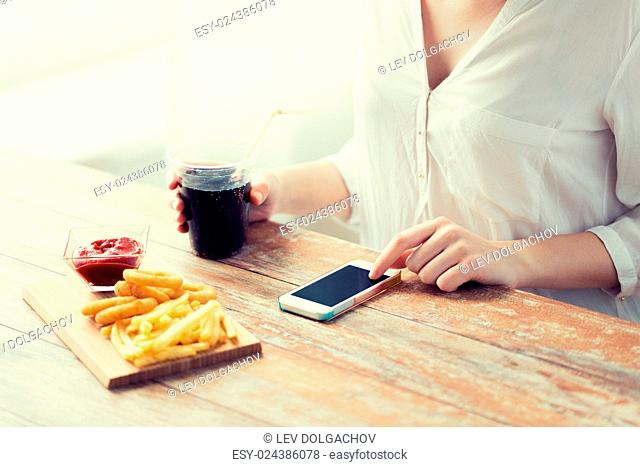 fast food, people, technology and diet concept - close up of woman with smartphone drinking cola and eating french fries