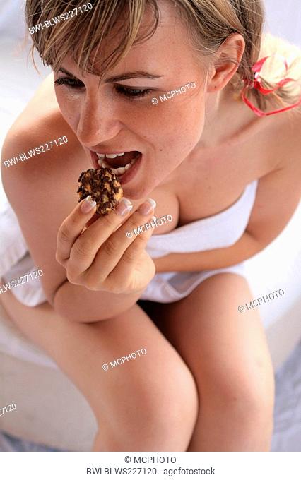 naked young woman veiling her breasts with a towel while putting a cookie into her mouth with lascivious exaggeration