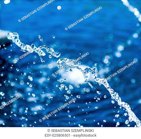 Abstract close-up of illuminated water stream and droplets suspended against blurred blue and white background