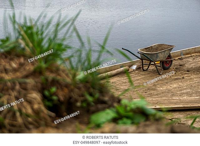 Wheelbarrow for construction in site building area at the river. Construction wheelbarrow and shovel in the sand by the river Daugava, Latvia