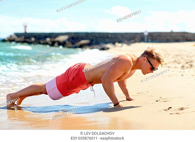young man doing push-ups on summer beach