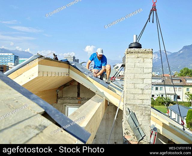Young man installing wooden plank on rooftop with crane machine