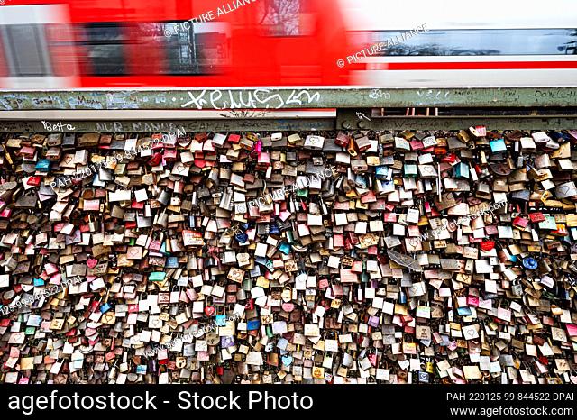 25 January 2022, North Rhine-Westphalia, Cologne: Numerous locks are attached to the Hohenzollern Bridge. A train passes behind it