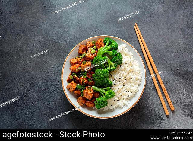 Sweet, spicy , crispy and fried Tofu in teriyaki sauce served in a bowl with broccoli, sesame seeds and rice. Healthy vegan food, gluten-free