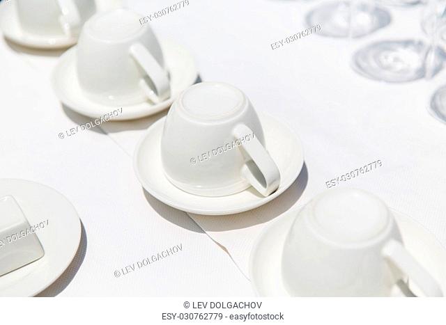 dishes, crockery and porcelain concept - white coffee cups upside down on saucers
