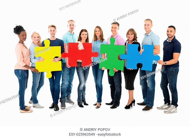 Full length portrait of creative business people holding jigsaw pieces against white background