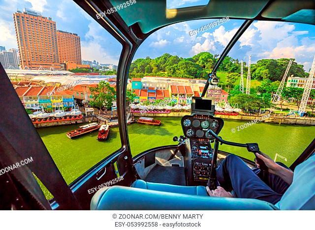 Helicopter cockpit interior flying on Clarke Quay and Riverside area in Singapore. Scenic flight above waterfront skyline with cruise boat on Singapore River in...