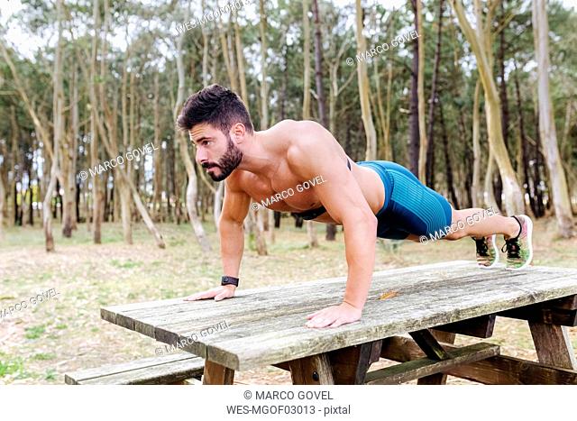 Barechested man doing push-ups on wooden table outdoors