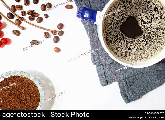On the table on a napkin is a Cup of black coffee, next to coffee beans and freshly ground black coffee. Top view, close-up