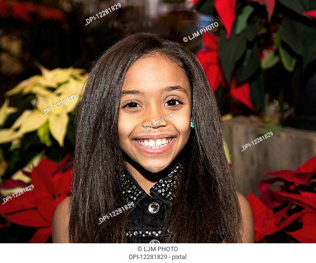 Young girl posing in front of poinsettia plants in a shopping centre; St. Albert, Alberta, Canada