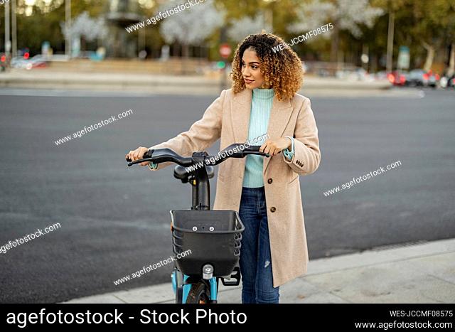 Woman with electric bicycle wheeling on footpath