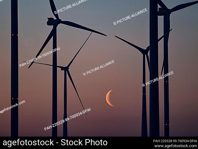 28 March 2022, Brandenburg, Sieversdorf: The waning moon is seen at dawn behind wind turbines in East Brandenburg. Photo: Patrick Pleul/dpa-Zentralbild/dpa