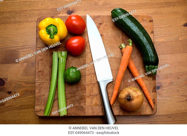 fresh vegetables on the cutting board and knife onion, tomatoes, carrot lemons., paprika, on wood background healthy