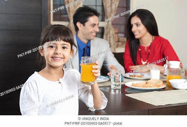 Portrait of a girl holding a glass of milk with her parents in the background