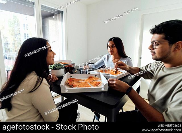 Young women and man having pizza at dining table in living room