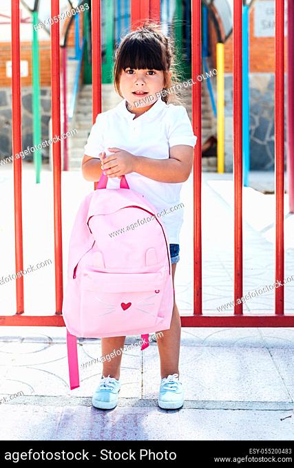 Brunette girl carrying a pink backpack at the entrance door of the school. School concept