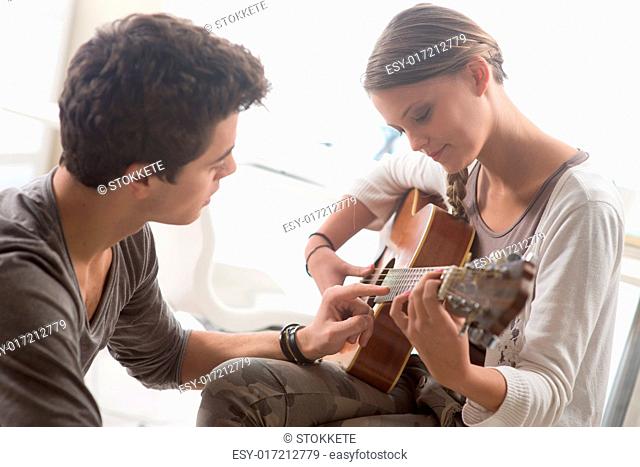 Young beautiful couple resting at home and playing guitar