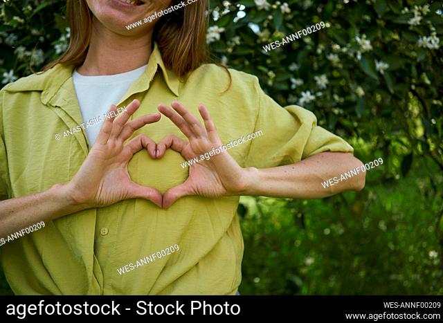 Woman making heart gesture on breast in garden
