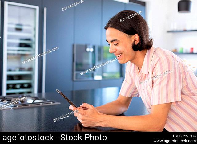 Happy biracial man using tablet in kitchen